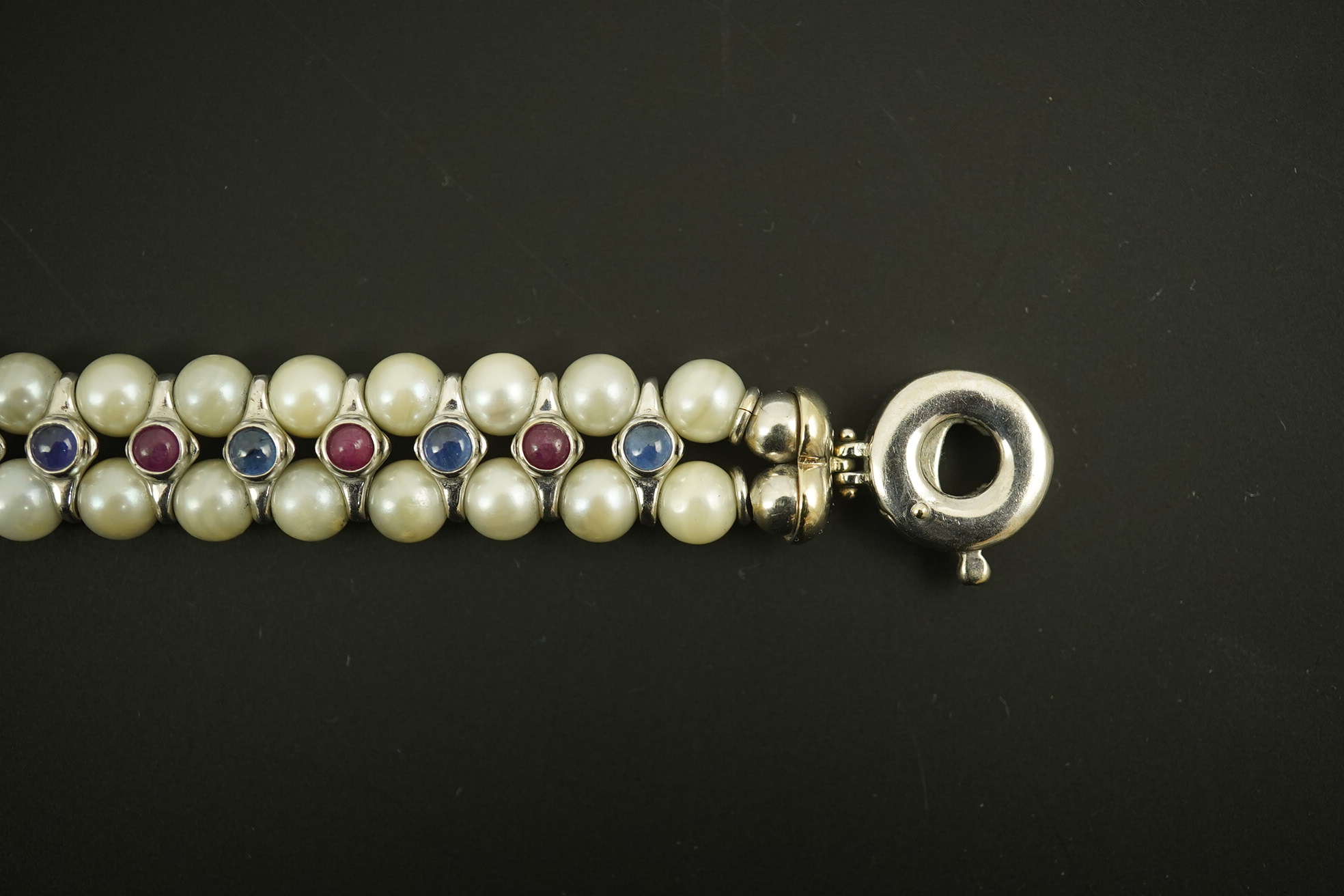 A late 20th century 18k white gold and two row cultured pearl bracelet, set with single row of cabochon rubies and sapphires